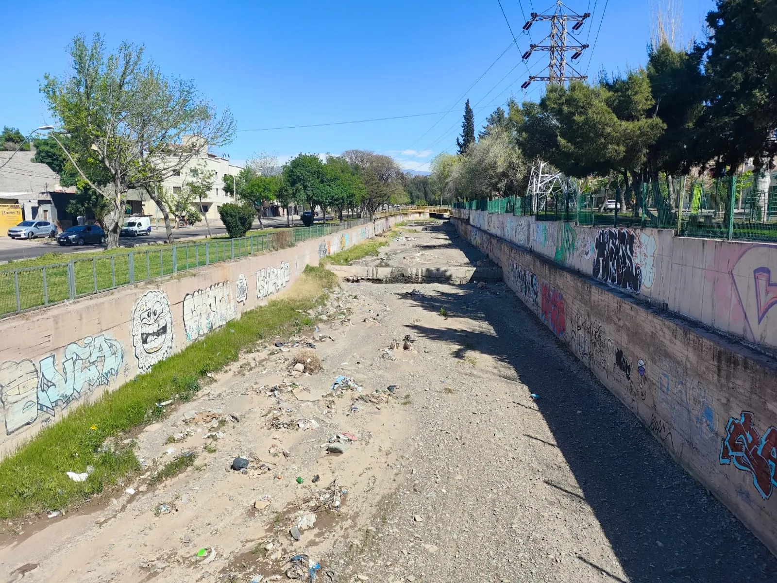 El Zanjón Frías hoy, visto hacia el oeste: lecho seco de ripio con basura, pasto y muros con graffitis